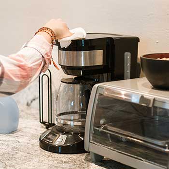Hand mit Lappen putzt die Oberseite einer Filterkaffeemaschine