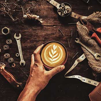 Hand mit Cappuccinotasse und Werkzeuge auf Tisch aus der Vogelperspektive